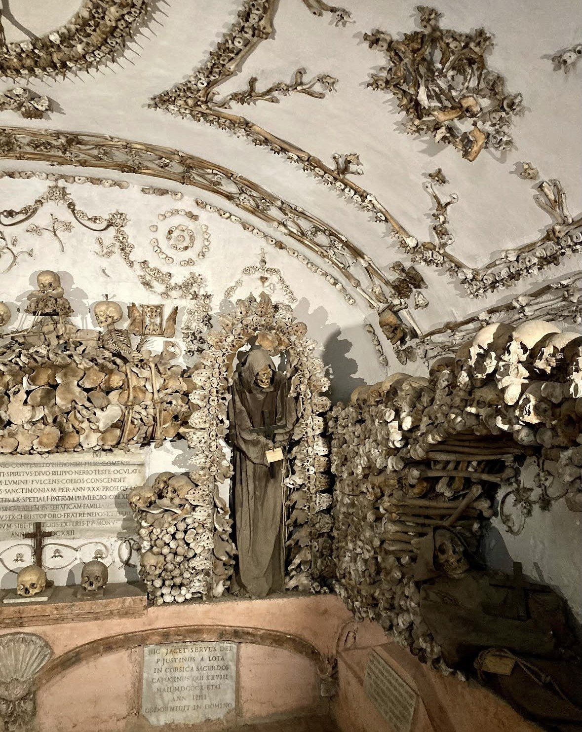 Vaulted bone chapel with Latin memorial slabs and hooded robed remains