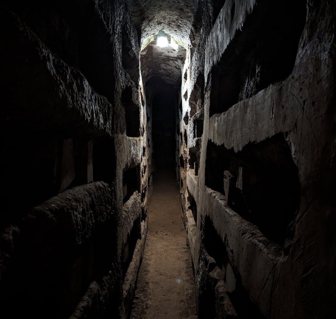Single lamp lighting a dark tunnel of empty graves in the Catacombs of Rome