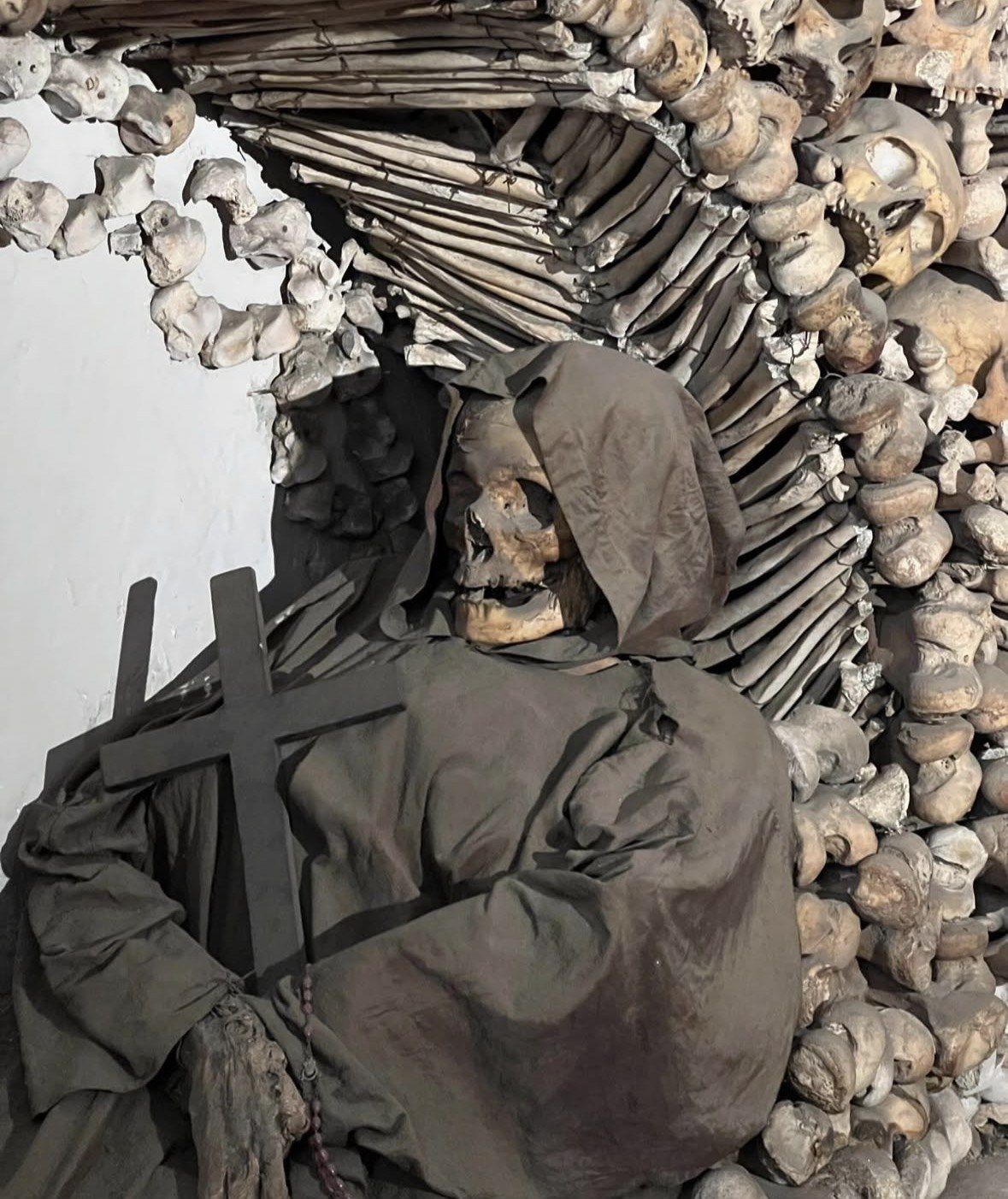 Hooded skeleton in a friar's habit holding a dark wooden cross