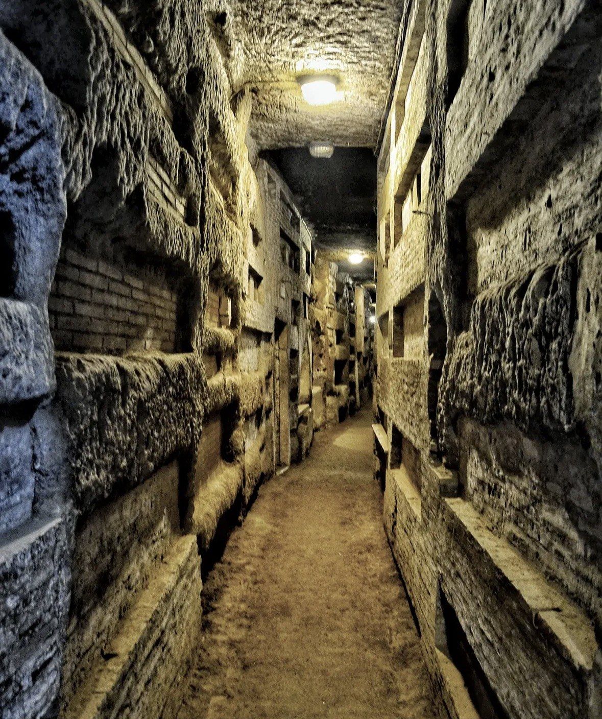 Lamp-lit tufa corridor lined with stacked empty burial niches underground