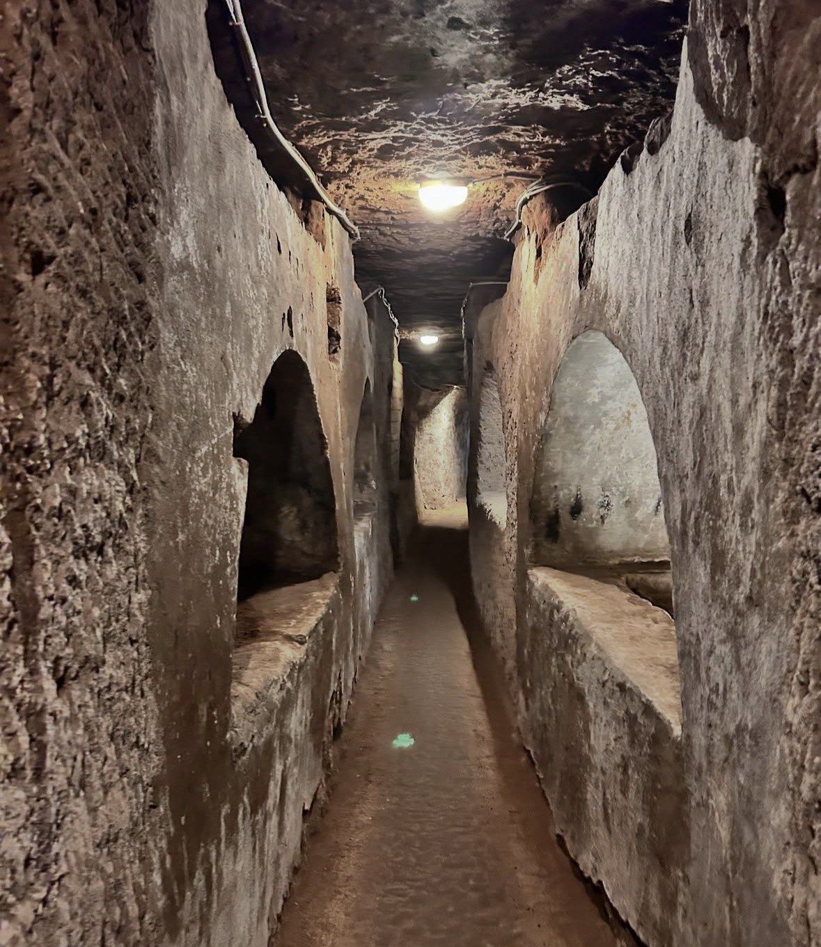 Narrow passage with arched grave recesses cut into pale tufa walls